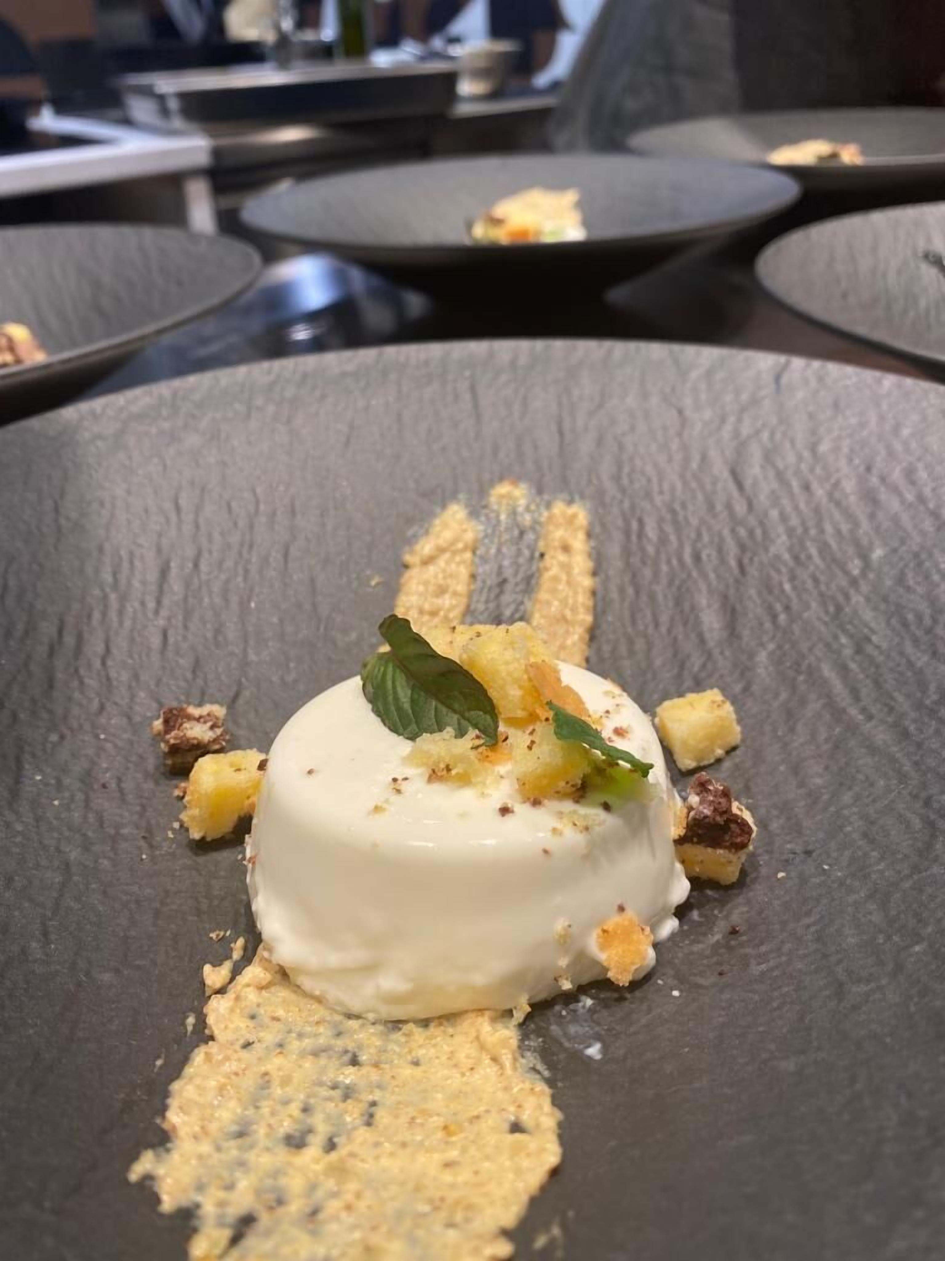 A dessert on a slate plate with crumbled cake pieces and a mint leaf garnish.
