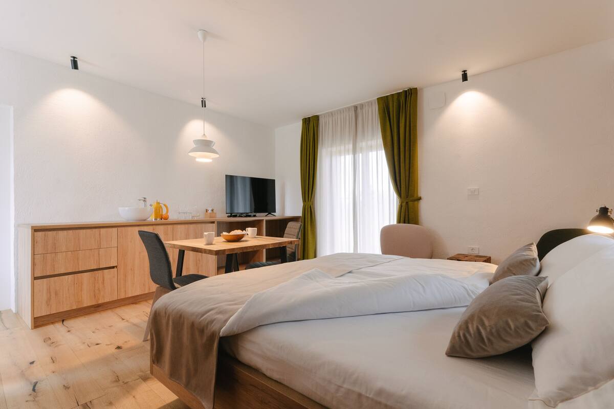 A modern hotel room with a bed, a desk, a chair, and a television.