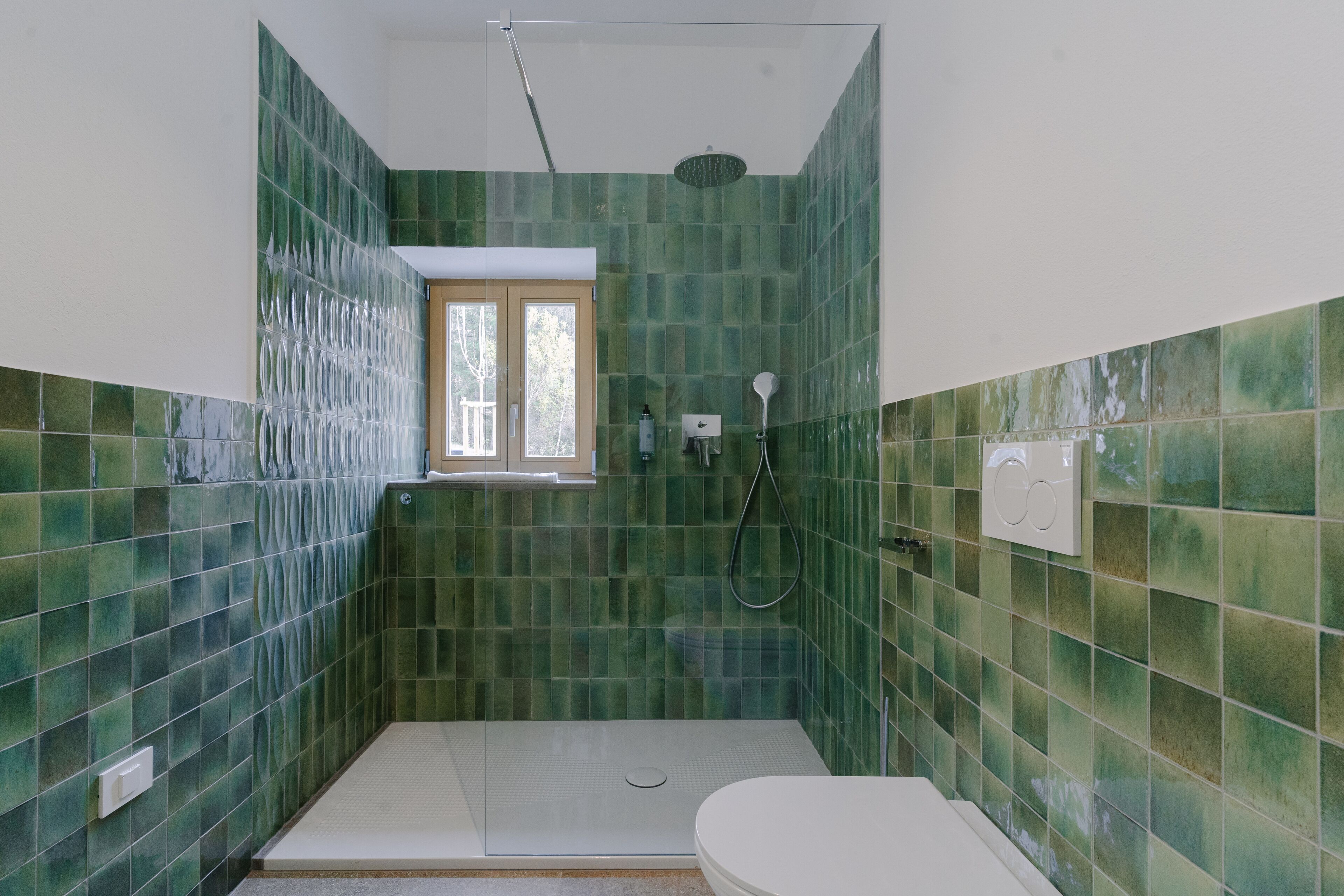 A bathroom with green tiled walls, a white toilet, and a shower area.
