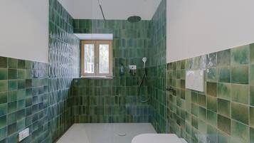 A bathroom with green tiled walls, a white toilet, and a shower area.