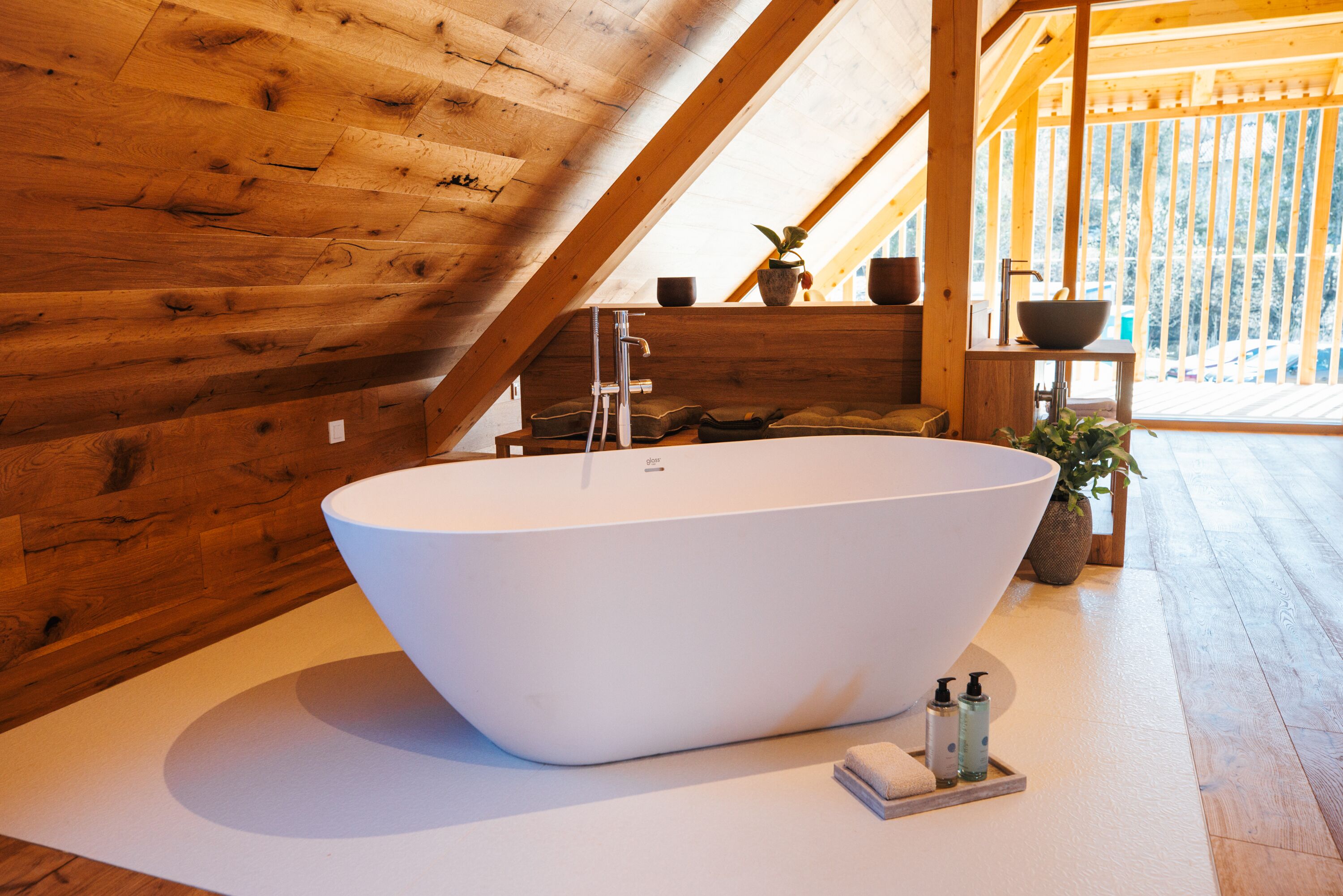 Un baño moderno con una bañera independiente, paredes de madera y vistas a un paisaje nevado.
