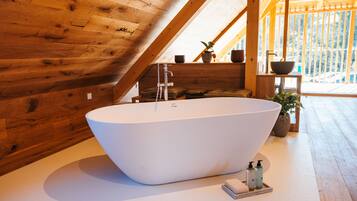Un baño moderno con una bañera independiente, paredes de madera y vistas a un paisaje nevado.