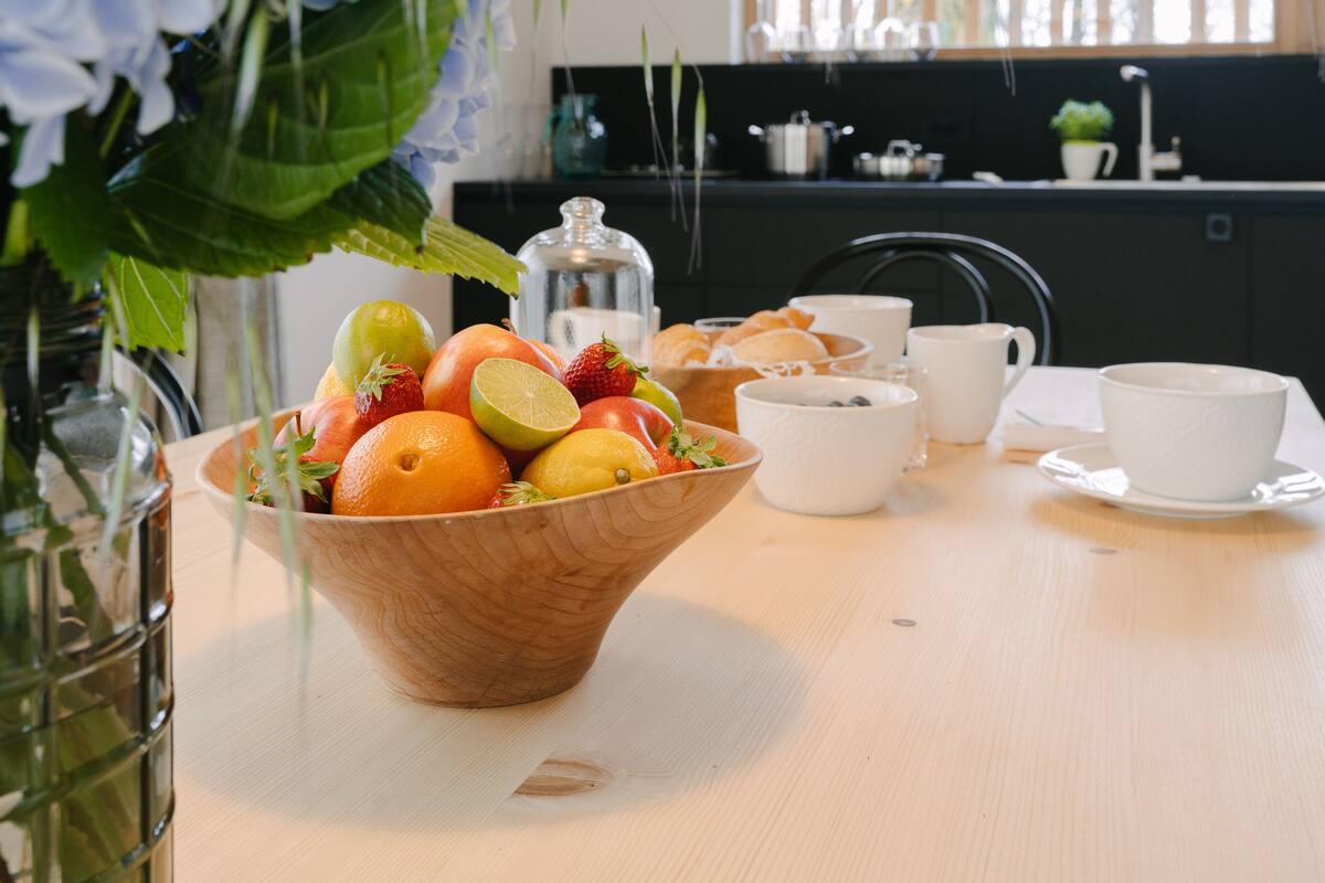 A wooden bowl filled with fruits and a white cup on a table.