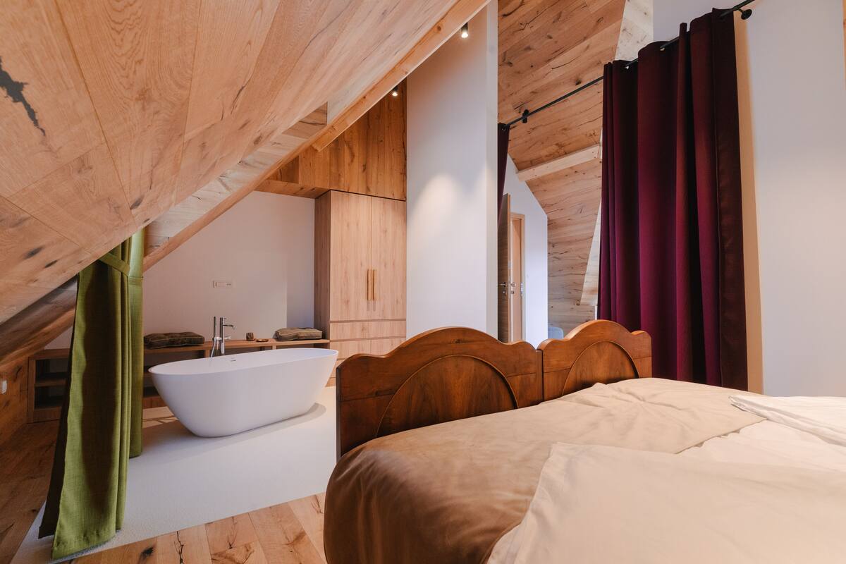 A bedroom with a wooden headboard, a large bed, a white bathtub, and a wooden ceiling.