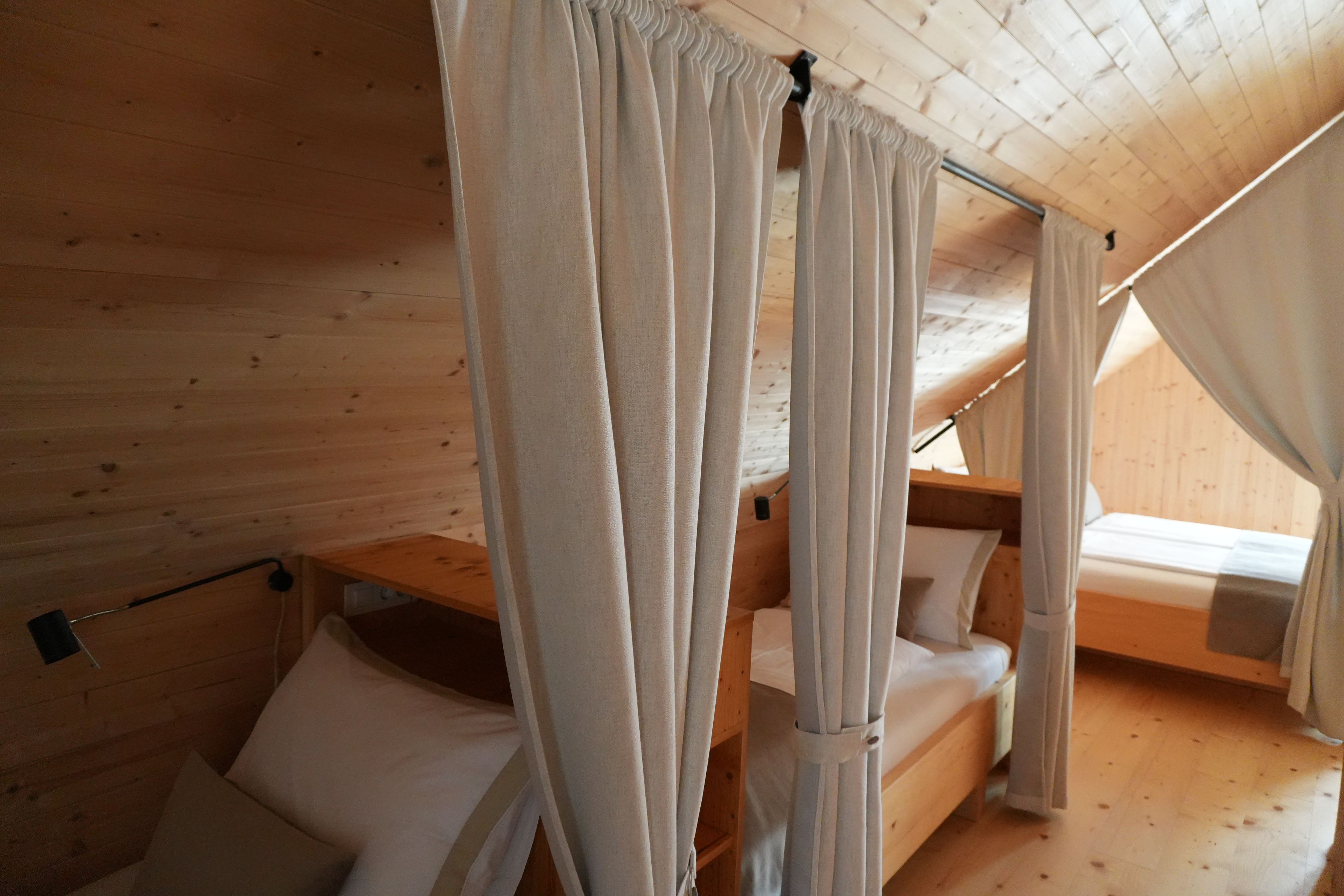 Une cabane en bois avec une chambre à l’étage aménagée dans un style loft, comprenant deux lits superposés, un lit à baldaquin et un plafond en bois.