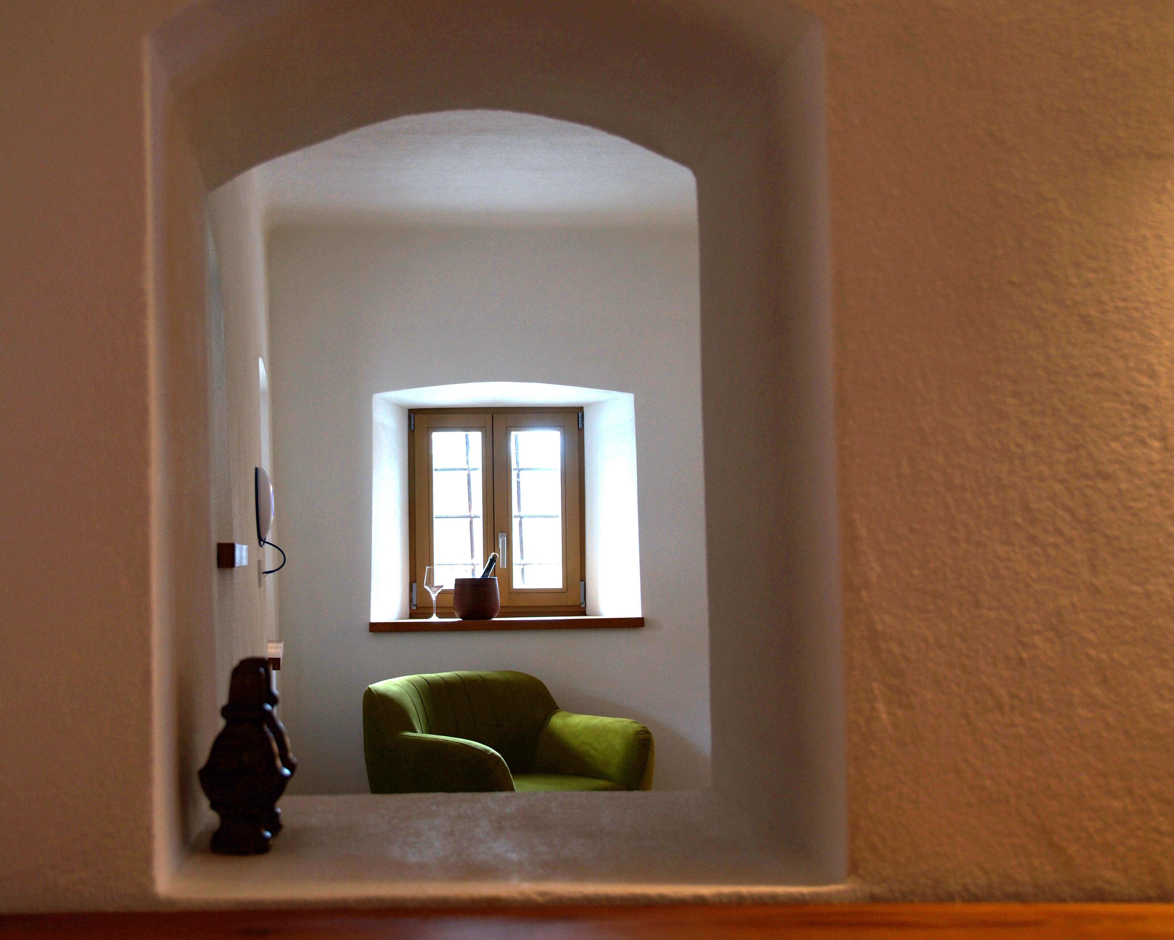 A room with a green armchair, a small table with a wine glass, and a window with two panes.