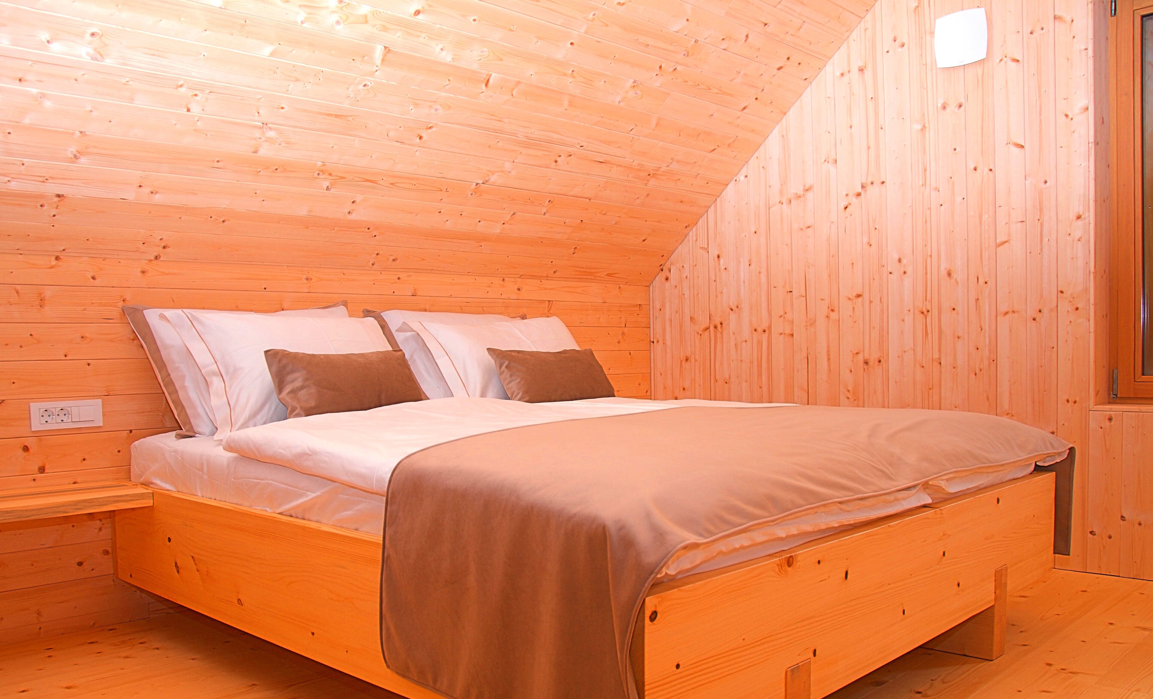 Ein Schlafzimmer einer Holzhütte mit einem Bett, Kissen und einem Nachttisch.