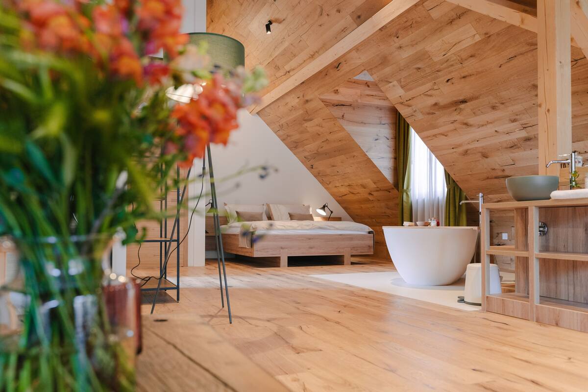 A modern bedroom with a sloped ceiling, a large bathtub, and a wooden floor.