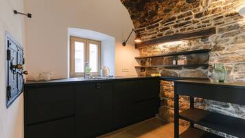 A kitchen with dark cabinetry, a stone wall, and a window.