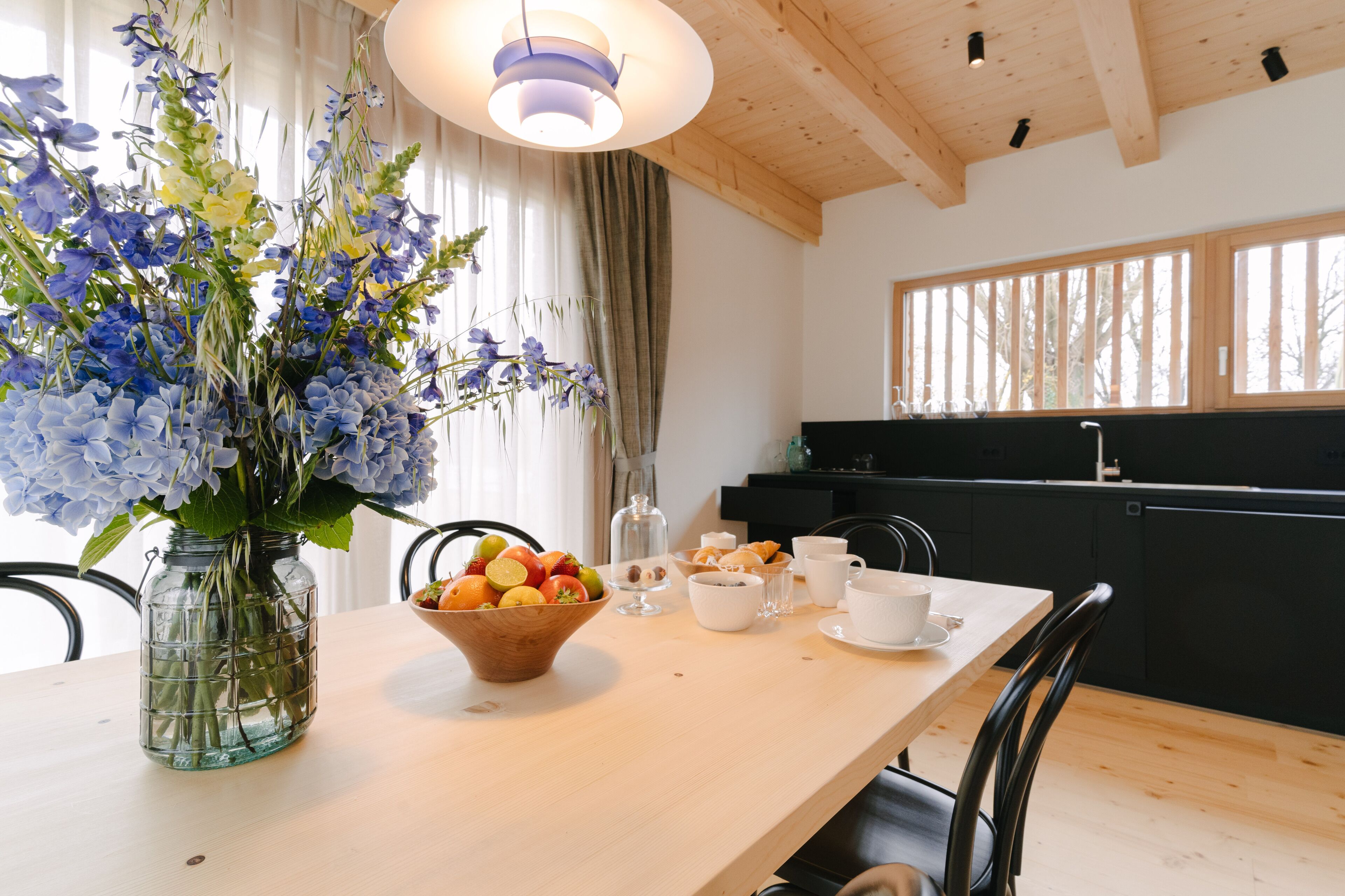 A dining area with a wooden table, a vase of flowers, and a bowl of fruit.