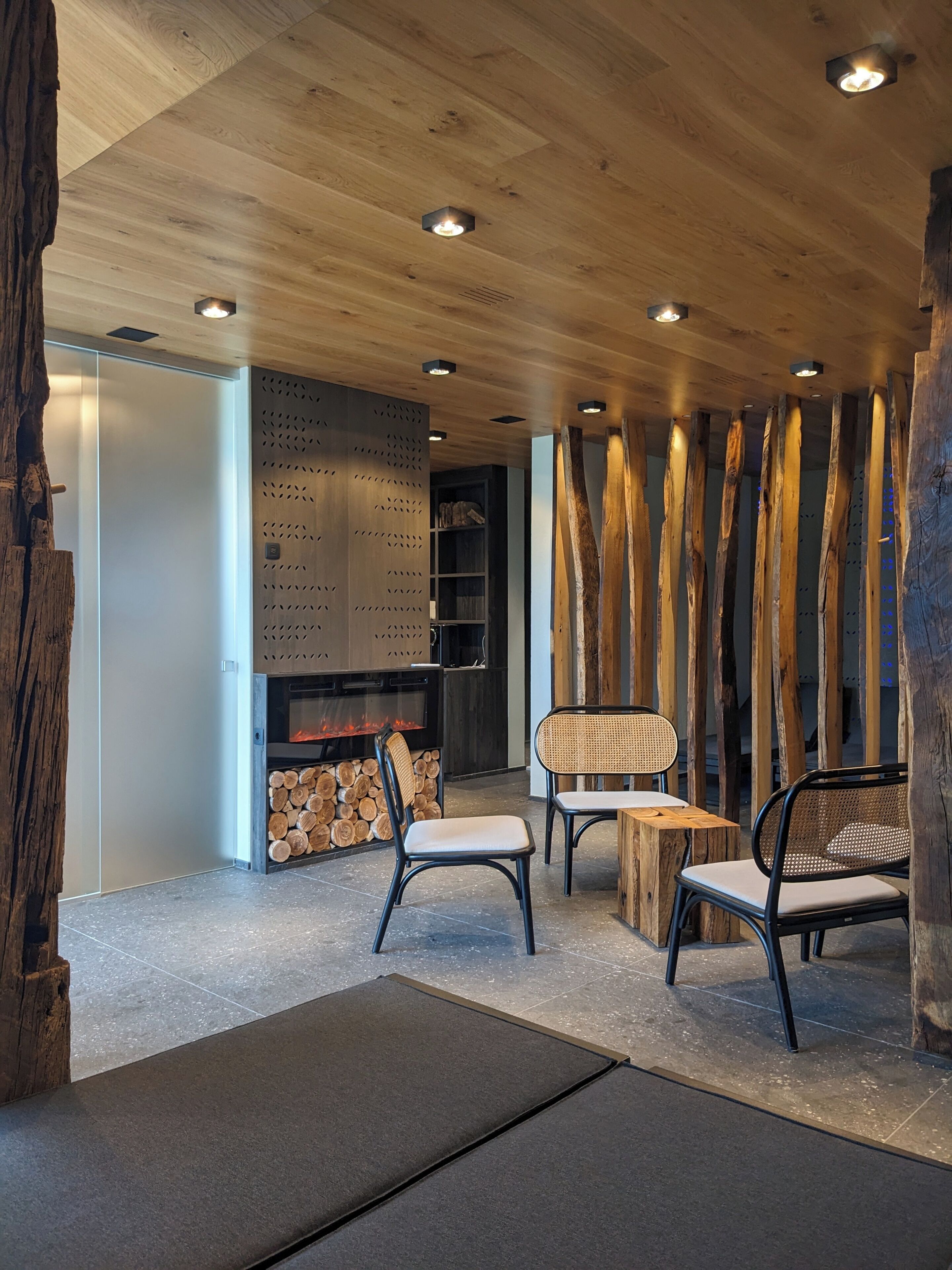 Un interior moderno con vigas de madera en el techo, una chimenea y dos sillones con respaldo trenzado.