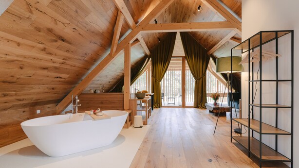 A spacious room with a large bathtub, wooden beams, and a view of the outdoors. - Pira Hotel (Postojna)