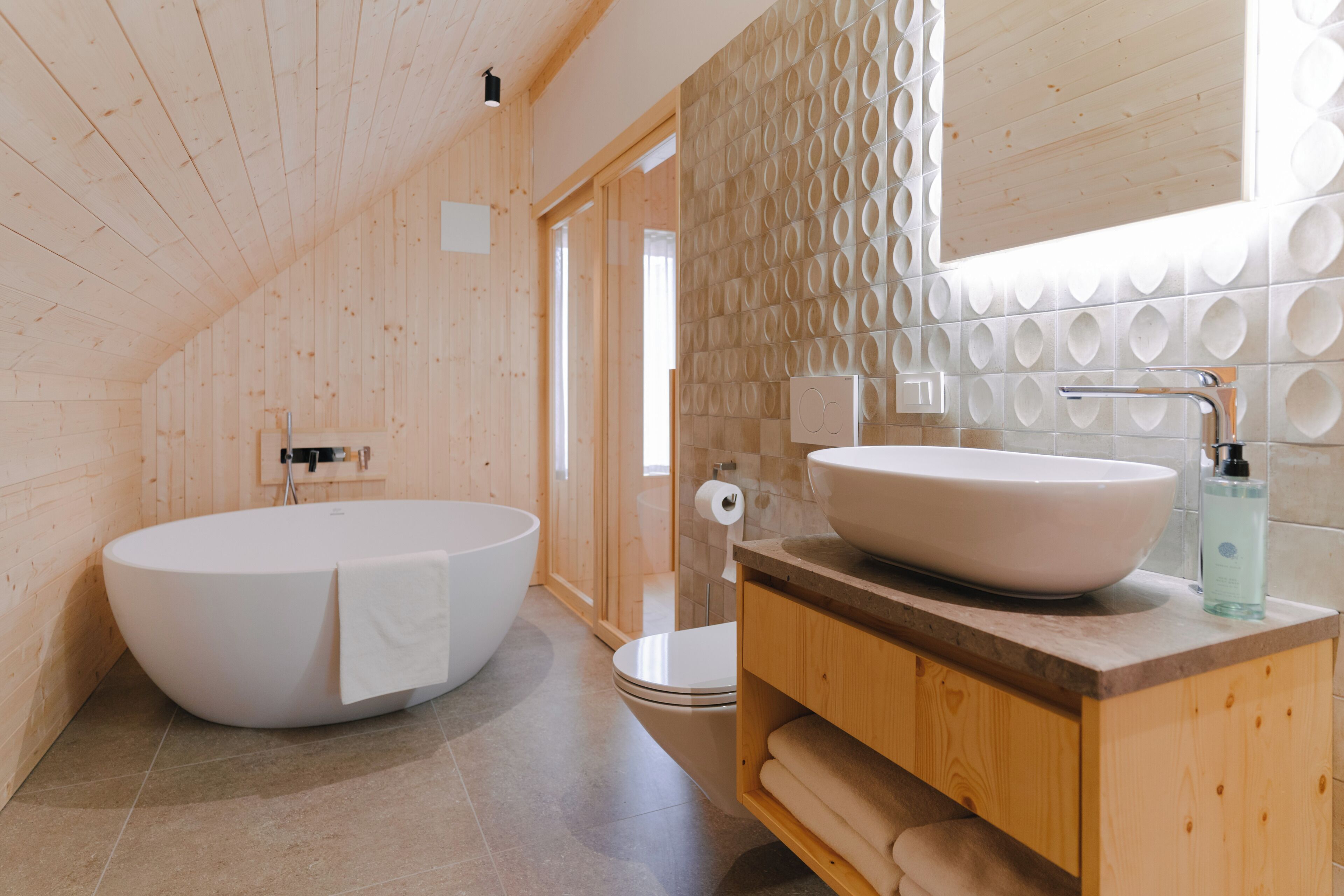 A wooden interior with a large bathtub, a sink with a mirror, and a toilet.