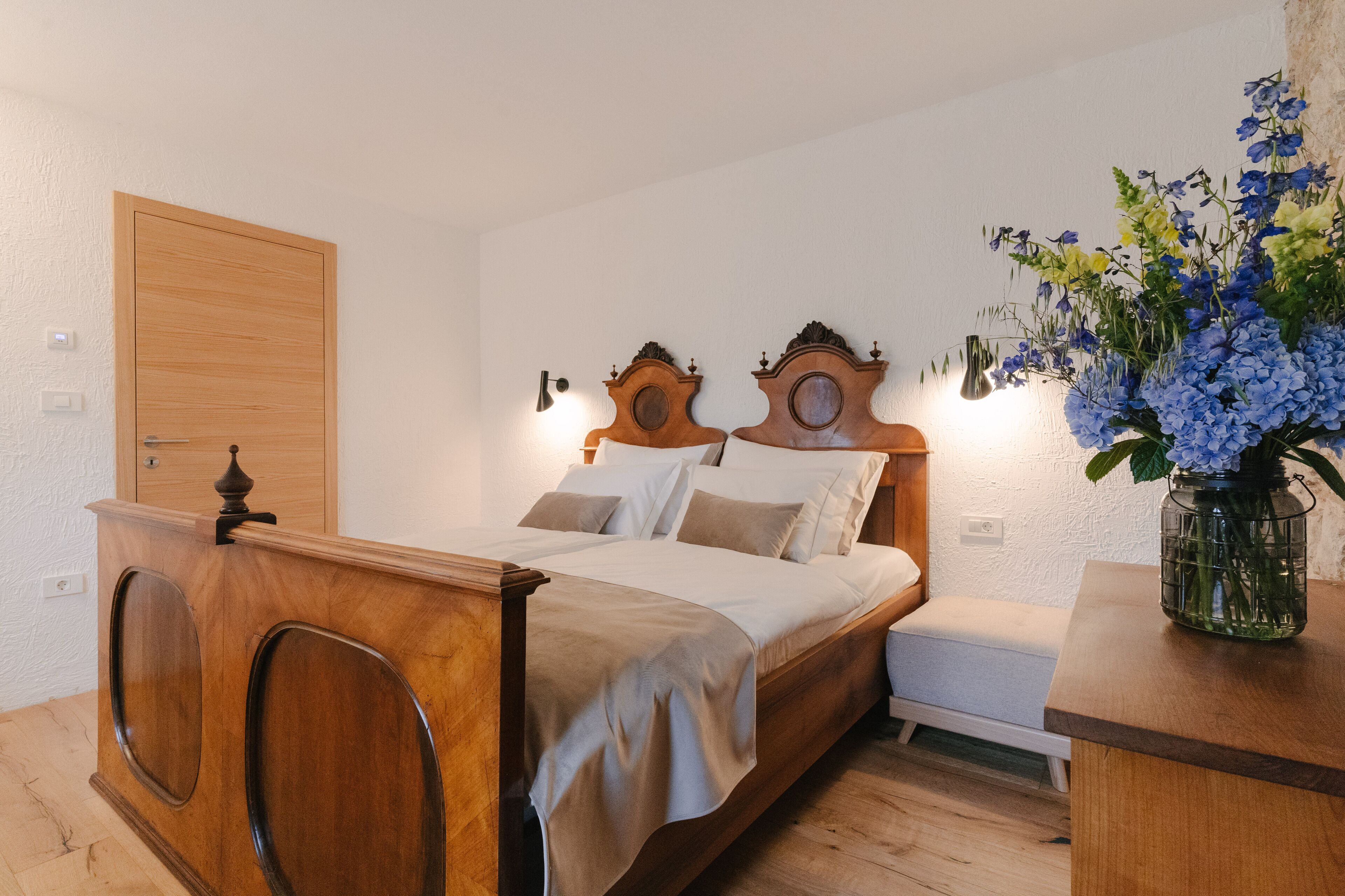 A bedroom with a wooden bed, bedside tables, a nightstand, and a vase with flowers.