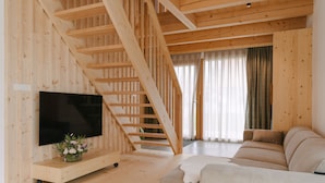 A wooden interior with a staircase, a flat-screen TV, a sofa, and a small table with flowers. - Pira Hotel (Postojna)