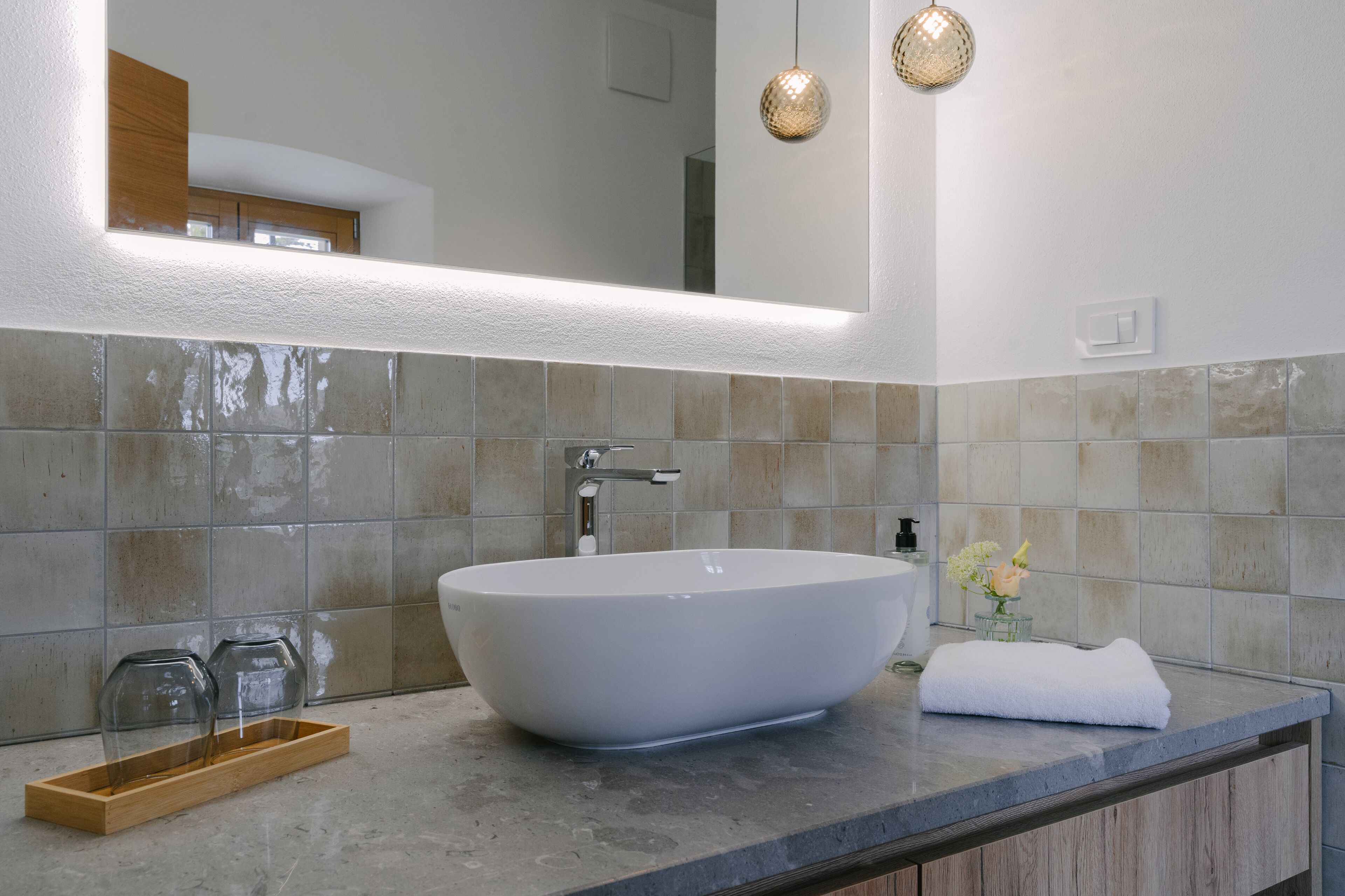 A modern bathroom with a large vessel sink, a wooden tray, and a towel on the counter.