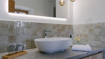 A modern bathroom with a large vessel sink, a wooden tray, and a towel on the counter.