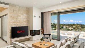 Un salon moderne doté d’un téléviseur à écran plat, d’une cheminée, d’un canapé et d’une grande fenêtre donnant sur une piscine et un paysage verdoyant.
