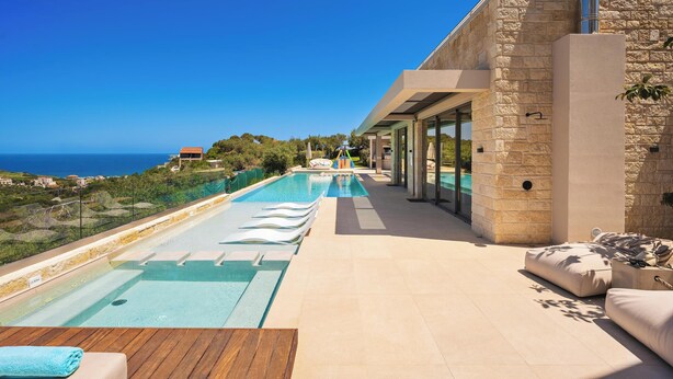 Un espace piscine moderne offrant une vue dégagée sur la mer, un bâtiment en pierre et une terrasse en bois.