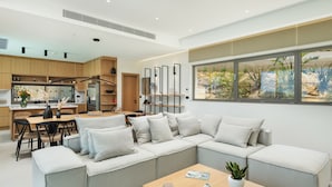 Un salon moderne avec un canapé d’angle gris, une table basse en bois et une grande fenêtre donnant sur un jardin.