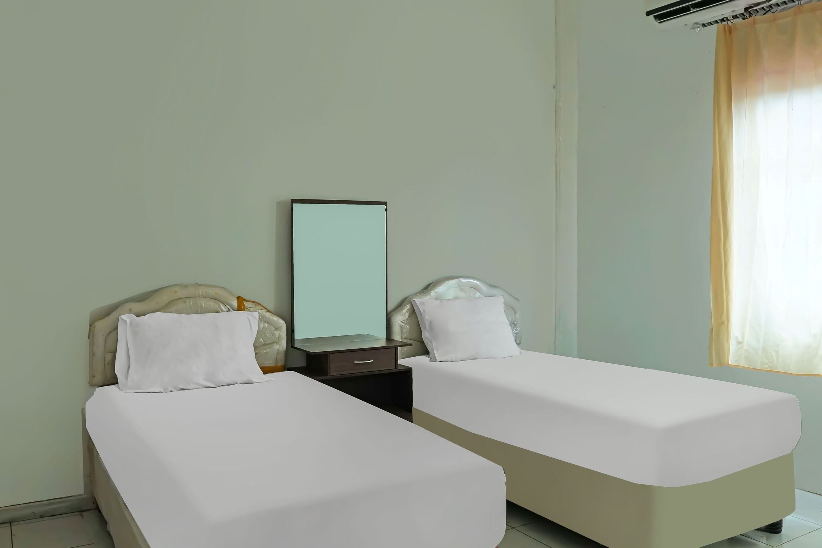 Una habitación de hotel con dos camas individuales, una mesita de noche con espejo y una ventana con cortinas.