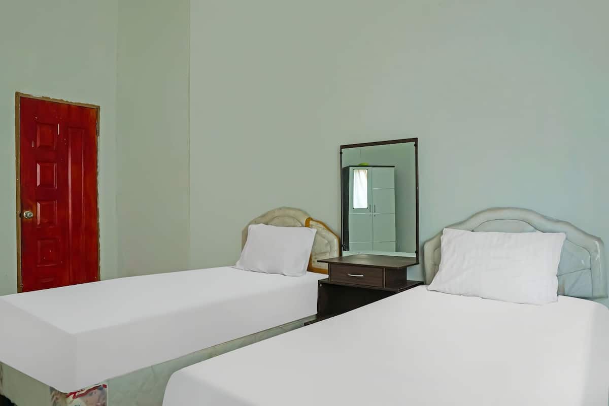 A room with two single beds, a red door, a mirror, and a small bedside table.