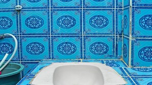 Un bagno con un WC integrato in una parete piastrellata, circondato da piastrelle blu con motivi floreali.