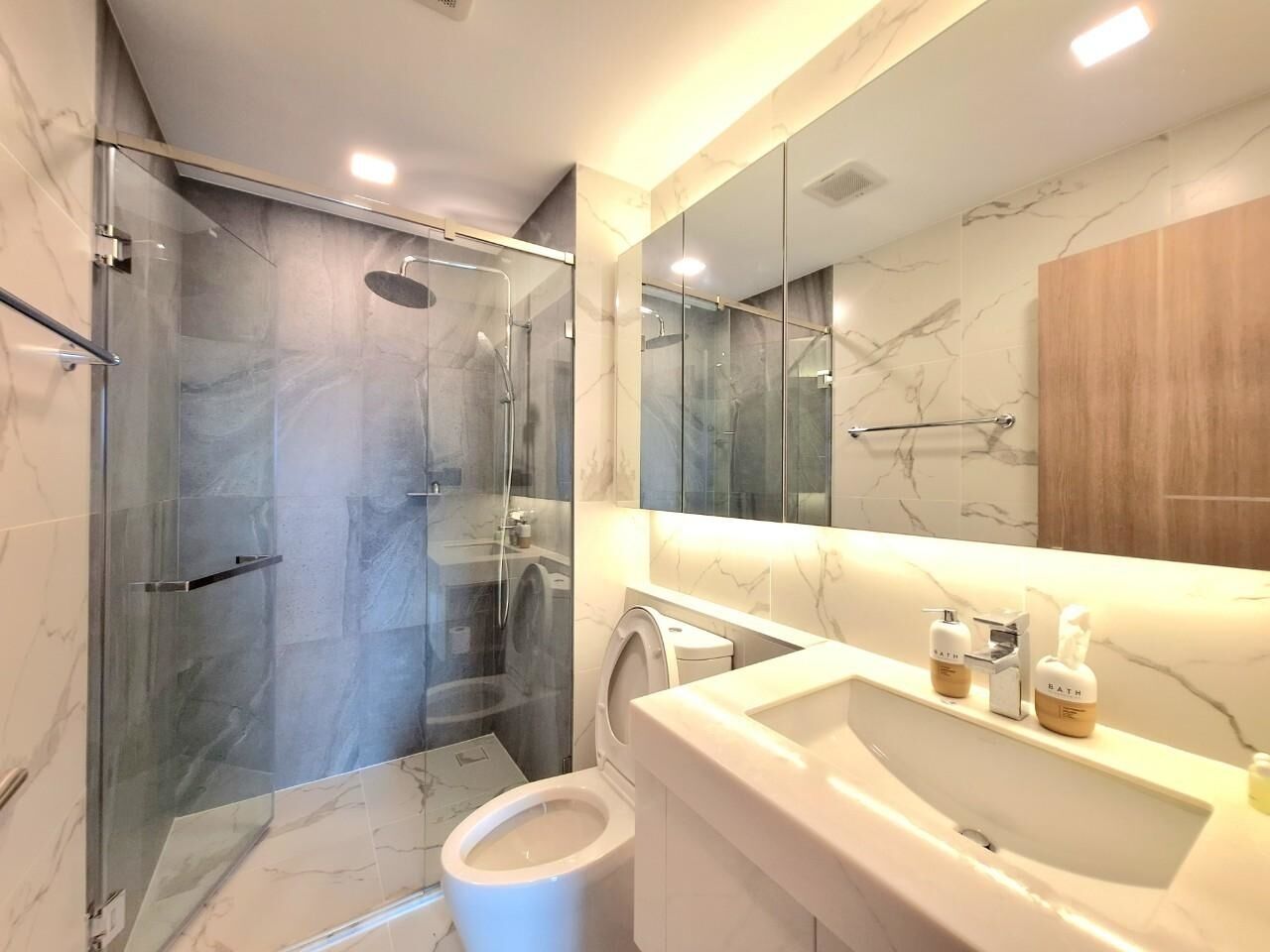A modern bathroom with a glass-enclosed shower, a white sink with a marble countertop, and a large mirror above the sink.