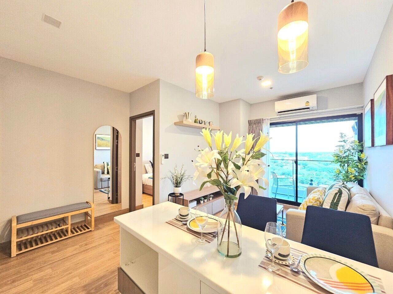 A modern dining area with a white table set for two, a vase of flowers, and a view of the sea through large windows.