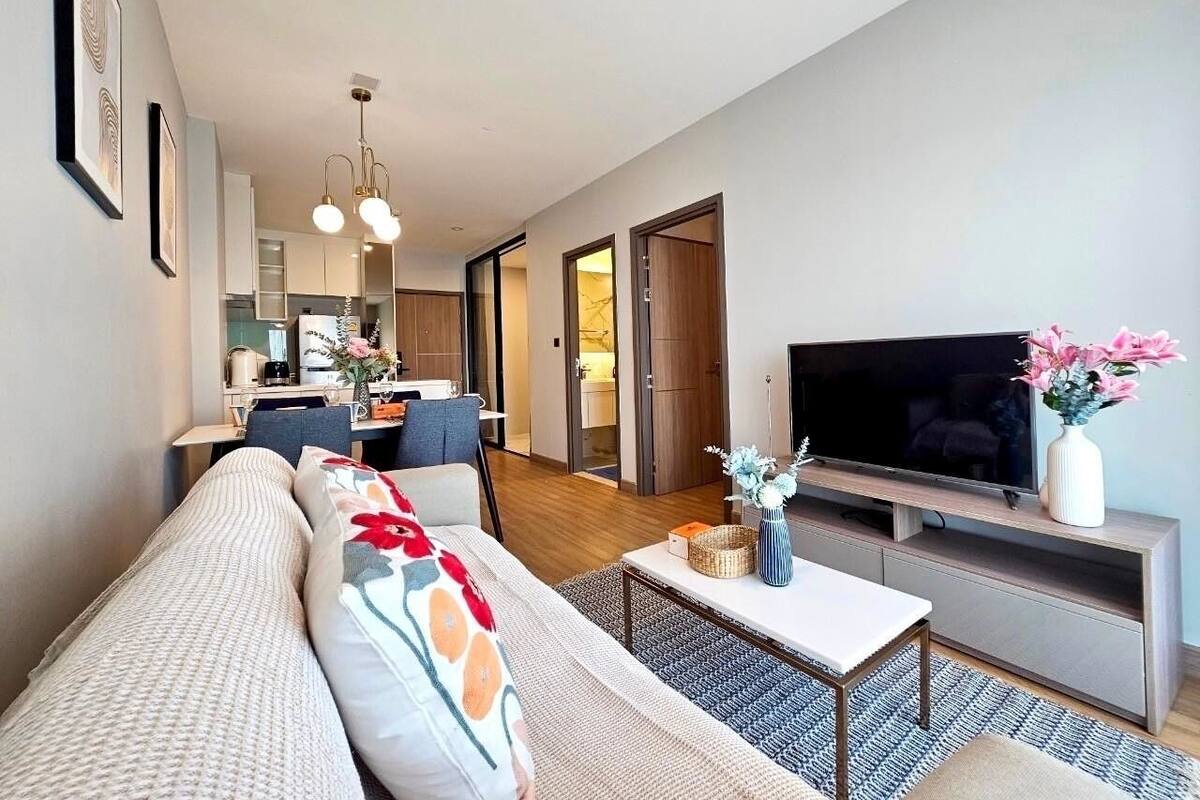 A modern living room with a sofa, TV, and a dining area in the background.