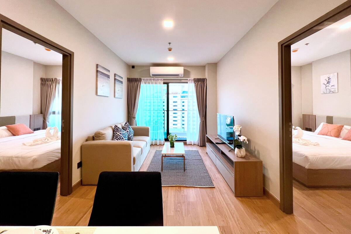 A hotel room with two beds, a sofa, a TV, and a dining table.