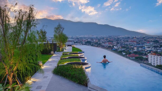 A man relaxing in a swimming pool with a cityscape and mountains in the background. - Astra Sky River Chiang Mai By Fang (Chiang Mai)