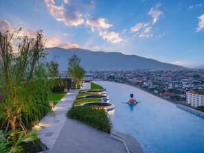 Un hombre se relaja en una piscina con un paisaje urbano y montañas al fondo.