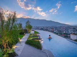 A man relaxing in a swimming pool with a cityscape and mountains in the background.