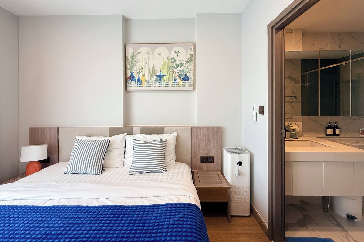 A hotel room with a bed, bedside table, lamp, and a painting on the wall.