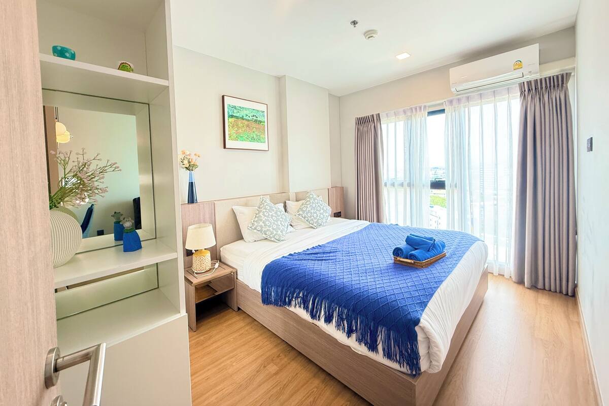 A hotel room with a bed, bedside table, lamp, and a window with curtains.