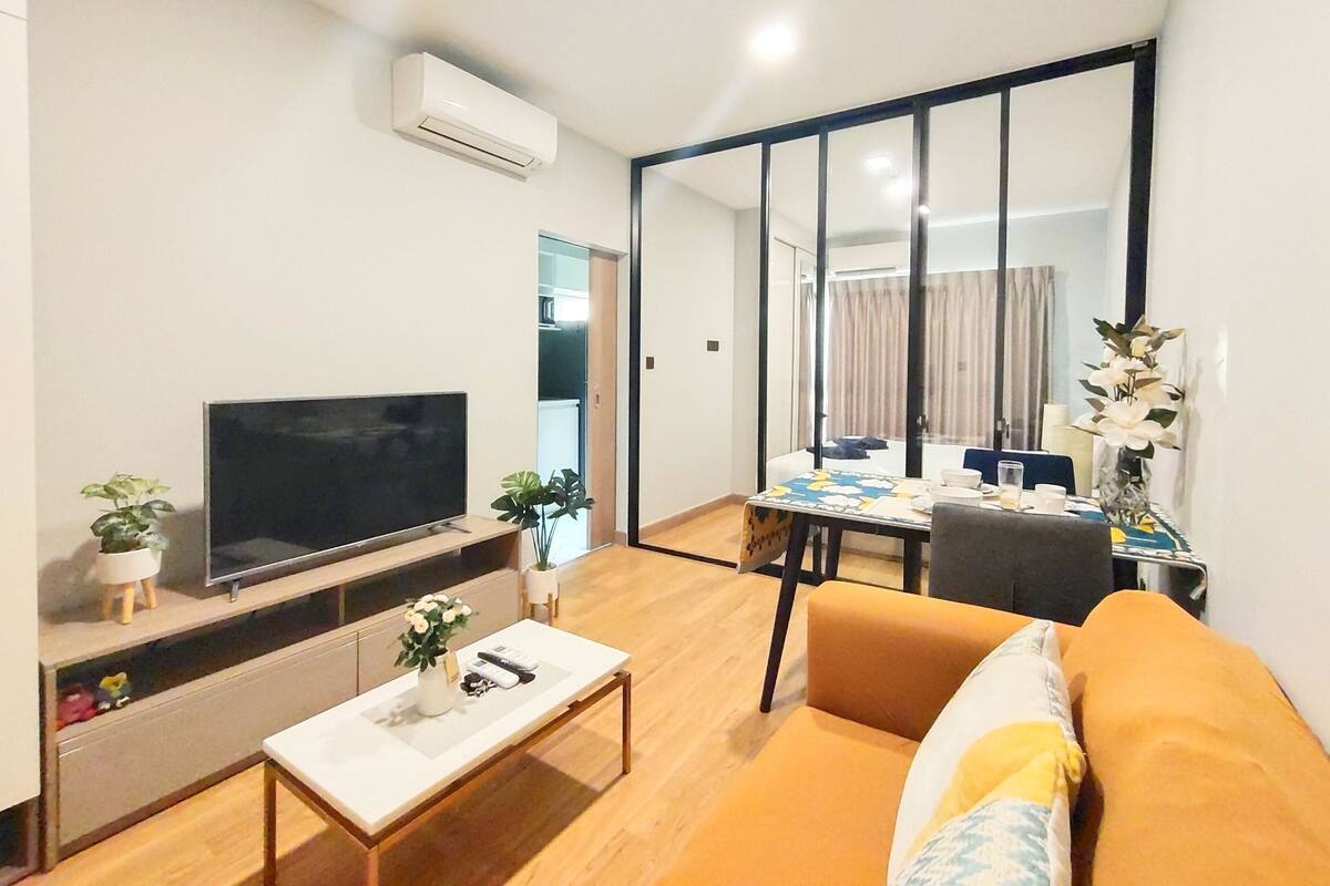 A modern living room with a flat-screen TV, a sofa, a coffee table, and a dining area with a table and chairs.