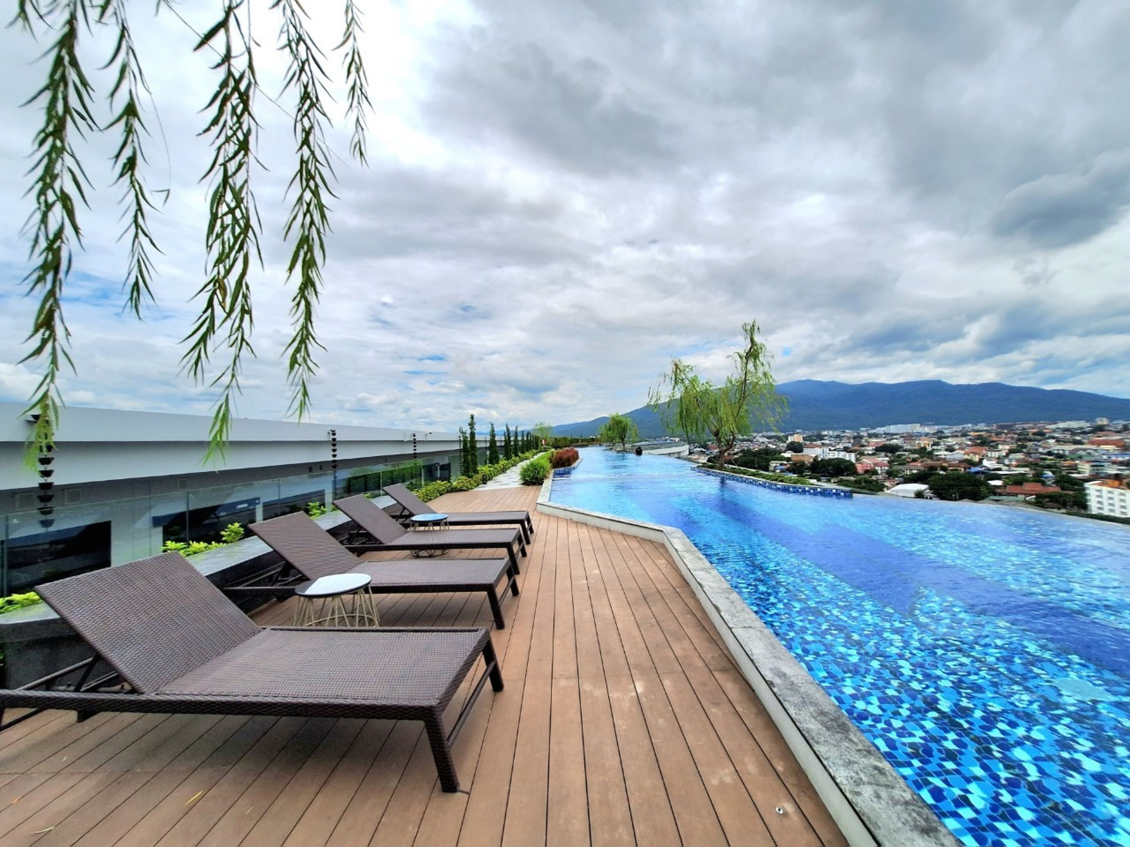 Una piscina infinita con sillones de descanso y vistas a un paisaje urbano y montañas.