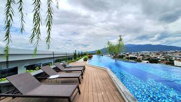 Una piscina infinita con sillones de descanso y vistas a un paisaje urbano y montañas.