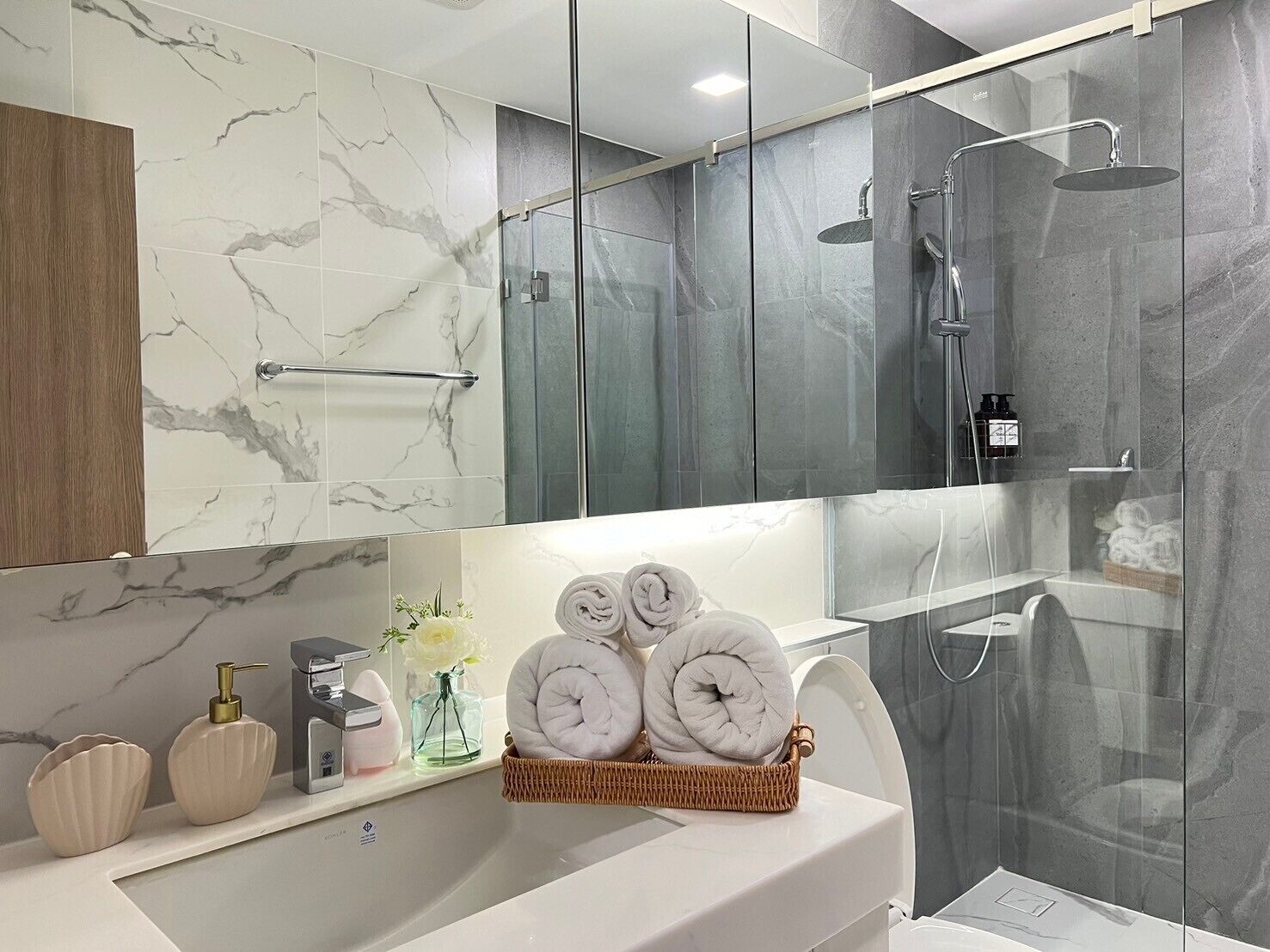 A modern bathroom with a marble vanity, a glass shower enclosure, and a wicker basket with towels.