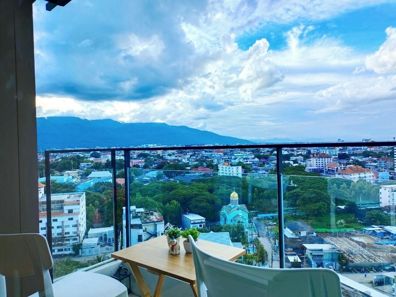 A room with a large window overlooking a cityscape, a table with chairs, and a small plant.