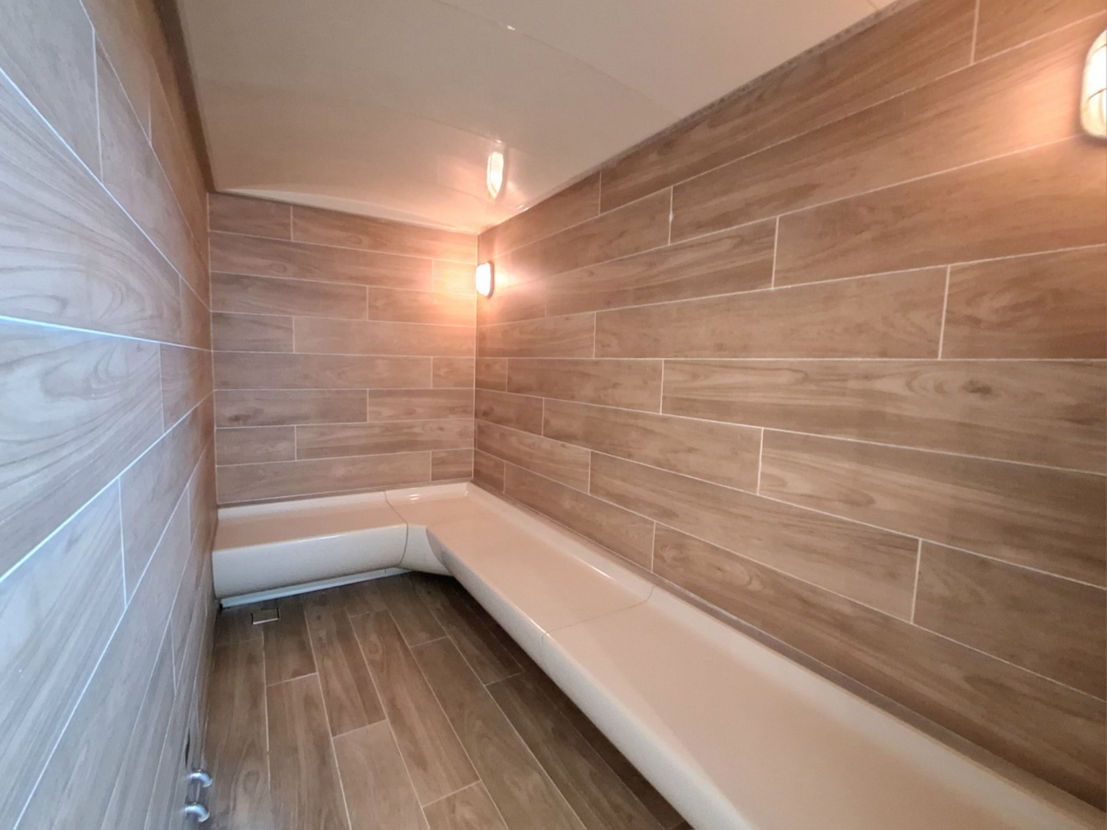 A modern bathroom with wooden wall tiles, a white bathtub, and a corner shower area.