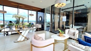 A modern hotel room with a large window offering a city view, a round table, and a seating area with white and gold furnishings. - Astra Sky River Chiang Mai By Fang (Chiang Mai)