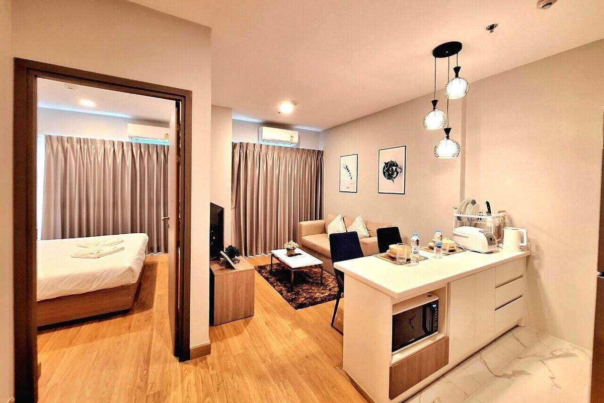 A modern hotel room with a bed, a sofa, a dining area, and a kitchen.