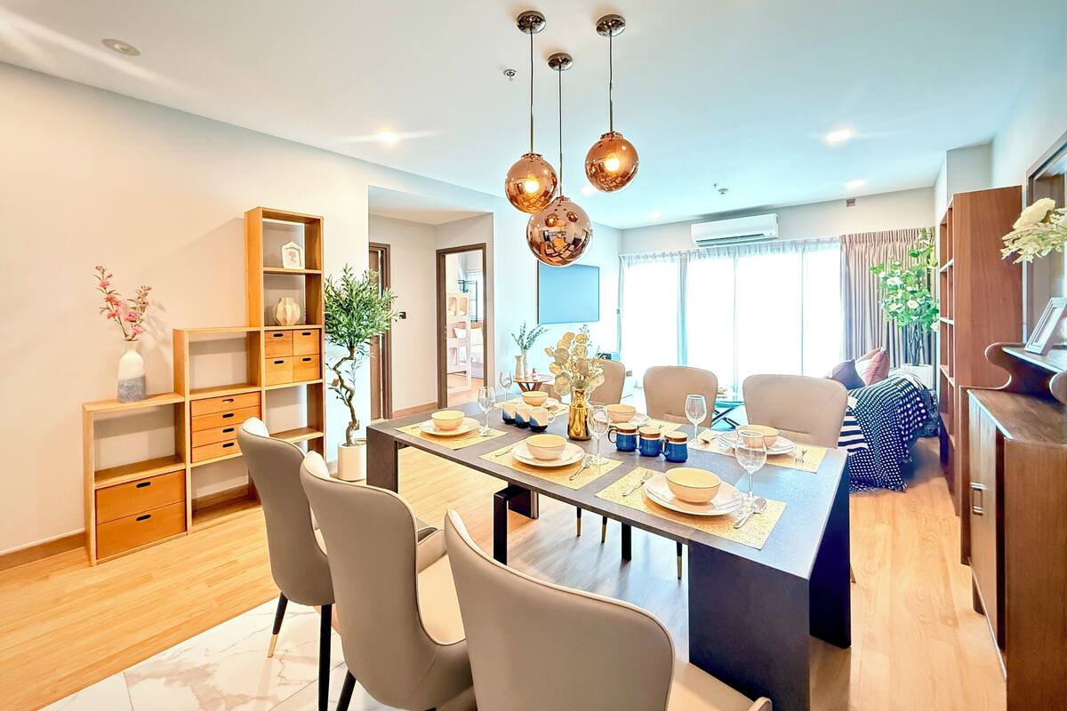 A modern dining area with a long table, chairs, and hanging spherical light fixtures.