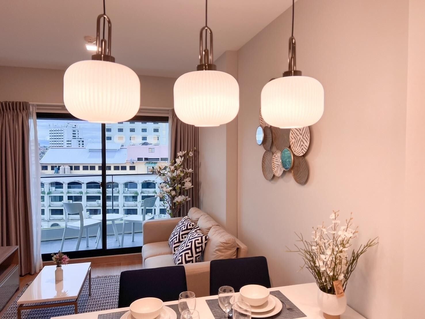 A modern hotel room with a dining area, a sofa, and a view of the cityscape through large windows.