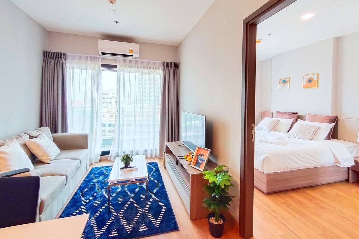 A modern hotel room with a sofa, a small table with a plant, a TV, and a bed with a wooden frame.