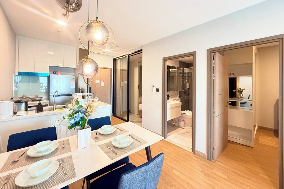 A modern kitchen with white cabinets, a dining area with a table set for two, and a glass-enclosed shower.