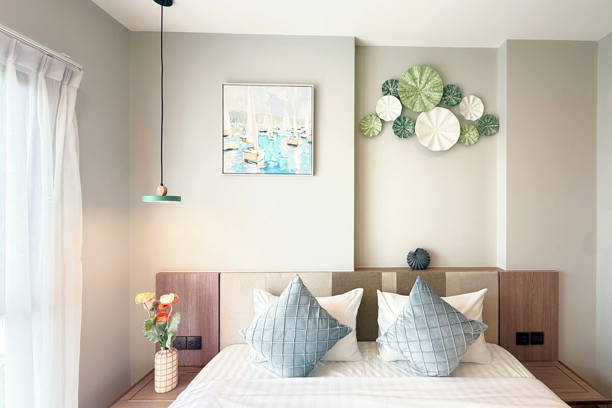 A modern bedroom with a bed, a nightstand, a vase with flowers, a wall-mounted artwork, and a decorative wall piece.