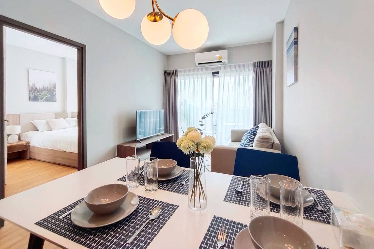 A modern hotel room with a dining area, a bed, a TV, and a view of the outdoors.